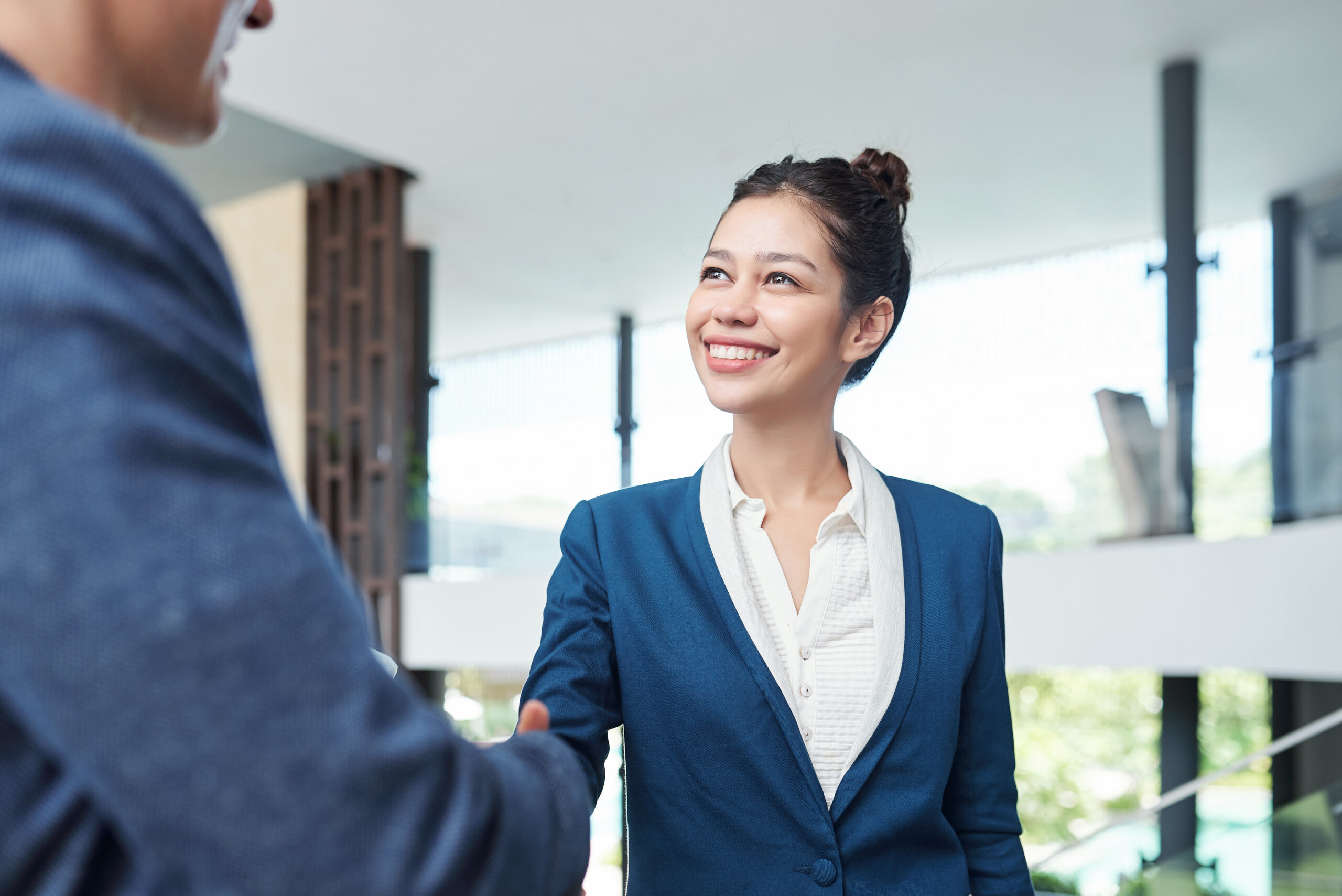 A young business professional shaking hands with a client in a modern office setting.