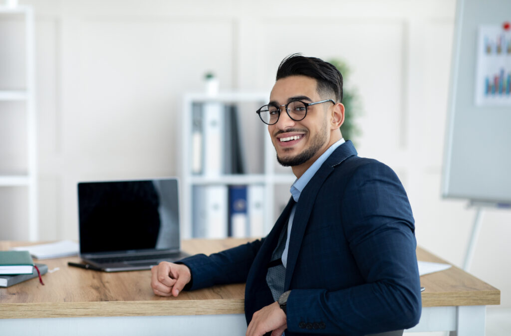 A young professional working in a minimalist office setting with a laptop on his desk.